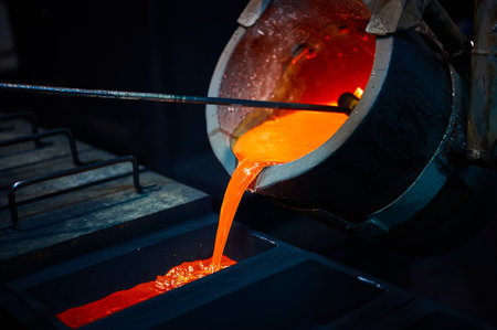 Pouring silver into graphite casting form in dark workshop