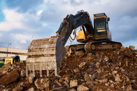 Bucket of excavator digs leftovers of destroyed buildingの写真素材