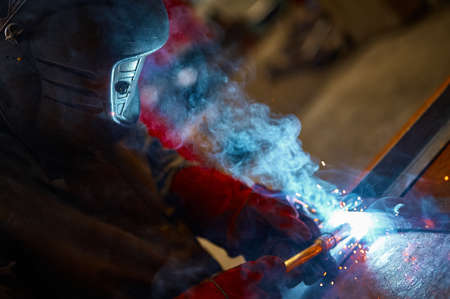 Employee in protective mask and gloves welds metal carcass
