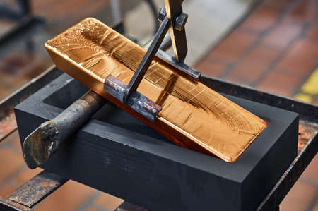 Gold ingot held by tongs in workshop of jewelry plantの写真素材