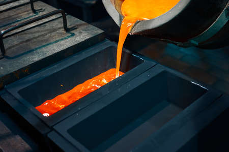 silver is poured from the ladle into a black rectangular graphite mold.の写真素材