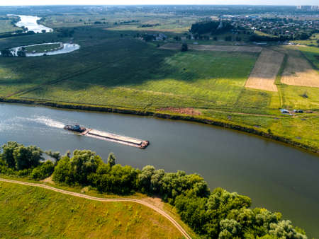 Towboat transports barge with sand along tranquil riverの写真素材