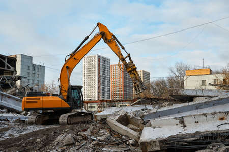Yellow excavator destroys armored concrete plates and beams