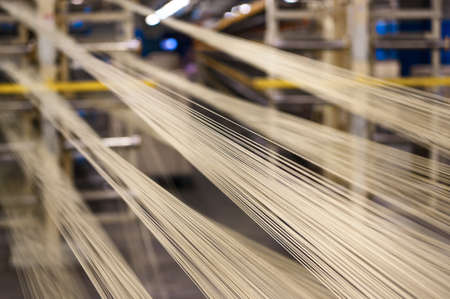 Metal cord yarn collector. Shiny cables for car tires reinforcement stretched in rolled steel workshop closeup. Material to build automobile tiresの写真素材