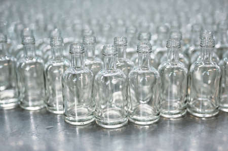 Lines of empty glass bottles for vodka drink at bright light in food and drink production plant...