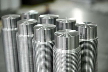 Collection of new shiny metal pins with screw thread on table in light storehouse of metalworking...