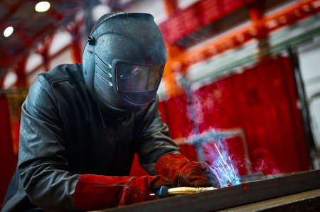 Employee in protective mask and gloves welds metal carcassの写真素材
