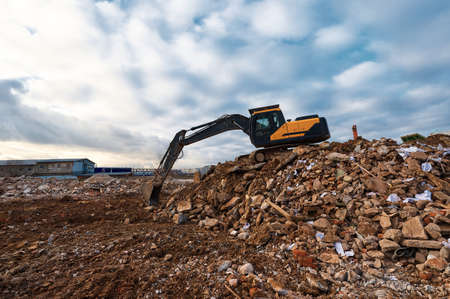 Excavator pours soil on pile of garbage at demolition site