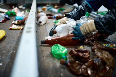 Worker sorts trash on conveyor belt at waste recycling plant