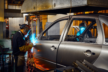 Worker in mask welds metal parts of auto carcass in shop