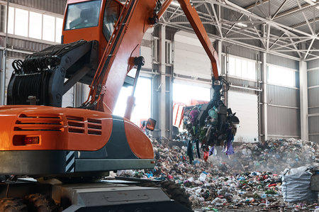 Grabbing excavator collects garbage in plant warehouse