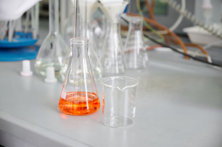 Laboratory experiment showing orange liquid in a flask beside a clear beaker on a lab table during a science research sessionの写真素材