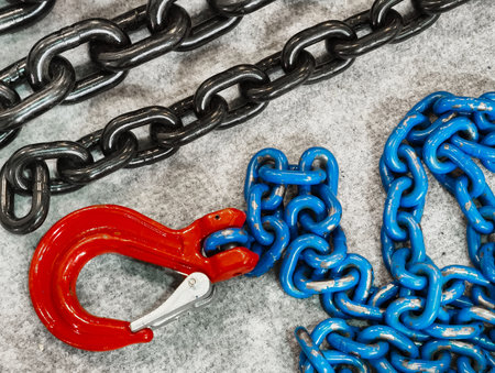 Industrial chains with a vibrant red hook showcasing strength and utility in a captivating arrangement on a textured surfaceの写真素材