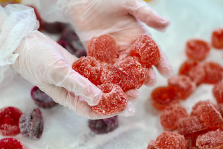 Enjoying sweet marmalade confections held in gloved hands at a confectionery shopの写真素材