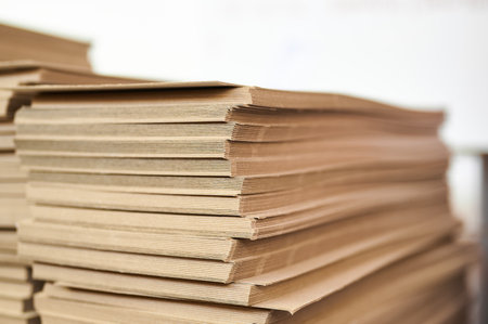 Stacks of thick paperboard ready for transformation into sturdy cardboard boxes within a bustling...
