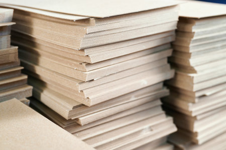 Stacks of thick paperboard prepared for crafting durable cardboard boxes in a bustling manufacturing...