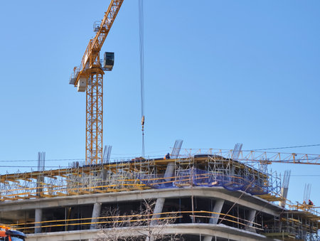 Construction site bustling with activity as crane lifts materials under clear blue skyの写真素材