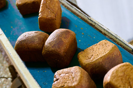 Freshly baked rye loaves cooling on a conveyor belt at a bustling bakery plant during morning production hoursの写真素材