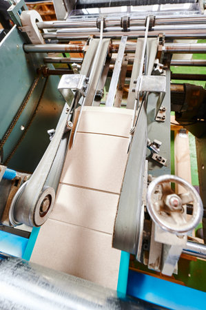 Efficient cardboard box flap folding machine in action at a bustling packaging facility