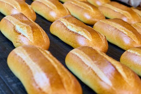 Freshly baked bread rolls exiting the bakery oven with a golden crust and soft texture in a bustling...