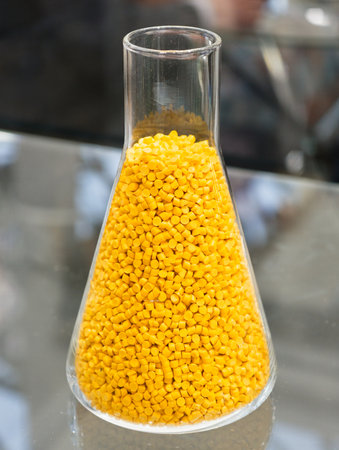 Bright yellow pellets fill a glass beaker, showcasing vibrant materials for creative projects in a studio settingの写真素材
