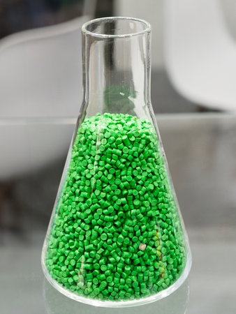 Vibrant green pellets fill a glass flask, showcasing the beauty of industrial materials in a...