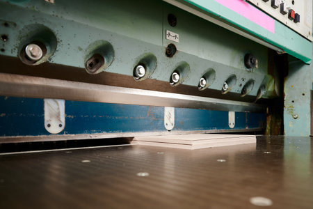 Cutting through layers of cardboard sheets with precision on guillotine shears in a bustling workshop environmentの写真素材