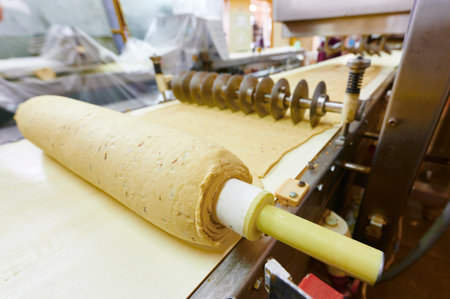Dough sheeting and cutting process in a bustling bakery with precision machinery at workの写真素材