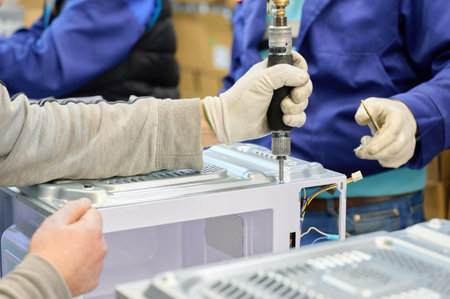 Workers assemble microwave ovens at a factory during a busy production shiftの写真素材