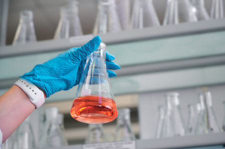 Scientist holds a flask with pink liquid in a laboratory filled with glassware during an experiment on a sunny dayの写真素材
