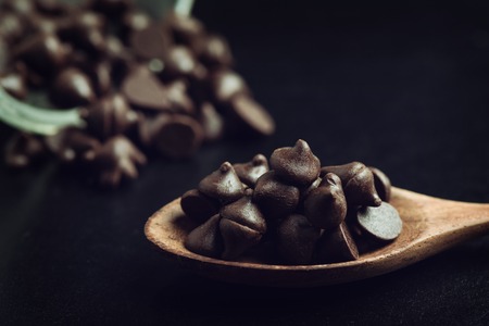 heap of dark chocolate chip in wooden spoonの写真素材
