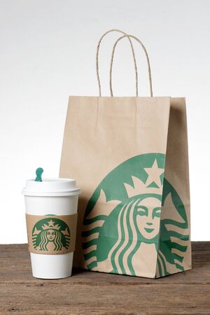 BANGKOK, THAILAND - FEBRUARY 26, 2015: White paper cup with sleeve with Starbucks logo and paper bag. Starbucks is the world's largest coffee house with over 20,000 stores in 61 countries.のeditorial素材