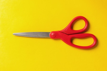 closeup red scissors isolated on yellow backgroundの写真素材