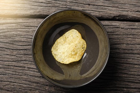 closeup last potato chip in bowl on wooden desk