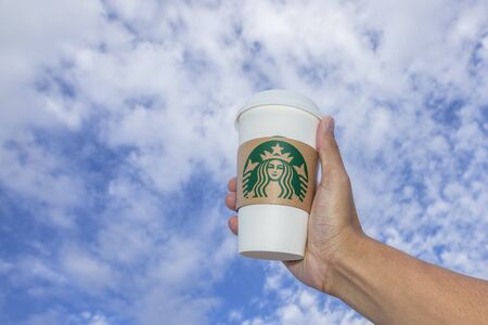 BANGKOK, THAILAND - MAY 22, 2015: White paper cup with Starbucks logo in hand against blue sky. Starbucks is the world's largest coffee house with over 20,000 stores in 61 countries.のeditorial素材