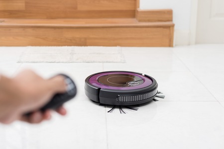 the man using remote control to control robotic vacuum cleaner on the floorの写真素材