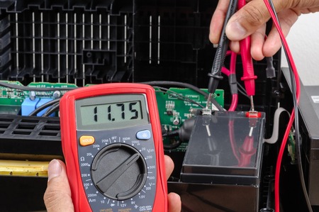 Technician measuring the voltage of battery for UPS (Uninterruptible Power Supply) with multimeter.の写真素材