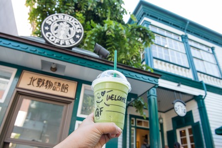 KOBE, JAPAN - MAY 18, 2016: Starbucks Green Tea Frappuccino in hand in front of Starbucks store in Kobe, Japan.のeditorial素材