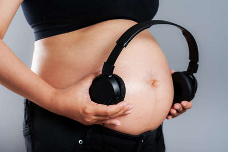 Pregnant woman holding headphones on her bellyの写真素材