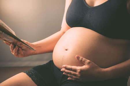 Pregnant woman reading a book, focused on her belly