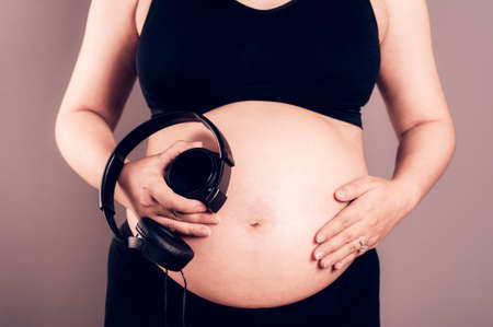 Pregnant woman holding headphones on her bellyの写真素材