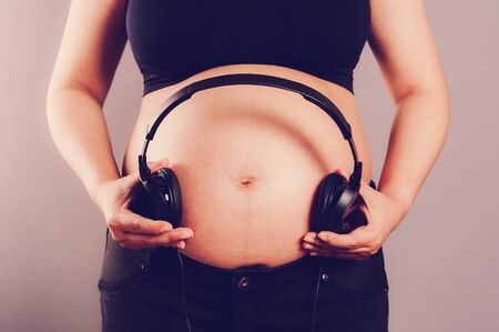 Pregnant woman holding headphones on her bellyの写真素材