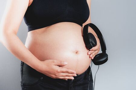Pregnant woman holding headphones on her bellyの写真素材