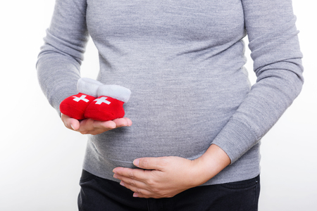 Pregnant woman holding red socks for baby.