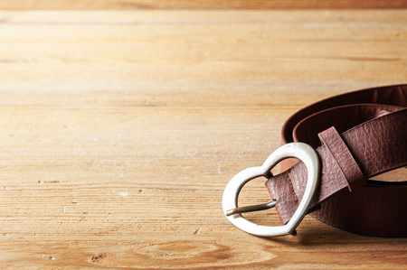 brown leather woman belt with metal heart shaped belt buckle on wooden board