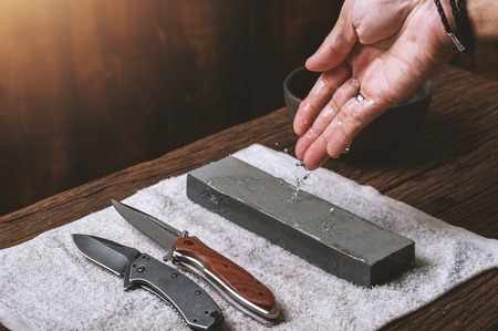 The man using whetstone to sharpening his pocket knife. Pocket knife care and maintenance concept.の写真素材