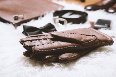 Pair of men's brown leather gloves and other men's accessories over white fur.の写真素材