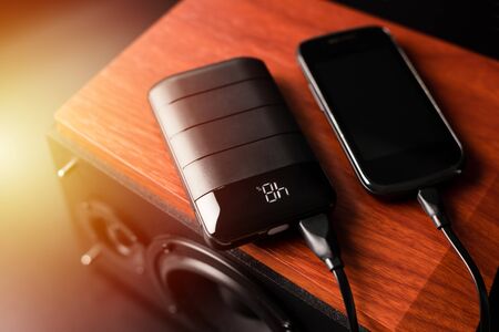 Charging the smartphone's battery with black power bank. Shallow depth of field focused on power bank display.の写真素材