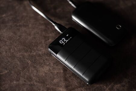 Black power bank connected with USB cable. Charging smartphone with power bank. Shallow depth of field focused on power bank display.の写真素材