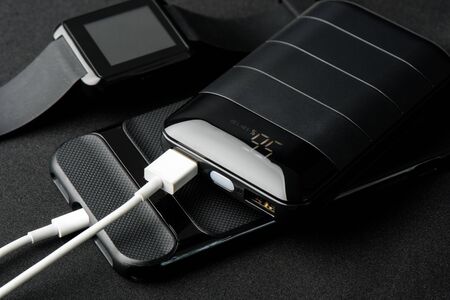 Charging the smartphone's battery with black power bank. Shallow depth of field focused on power...